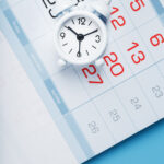 Annual calendar with a white alarm clock on a blue background. The concept of the passage of time and significant dates